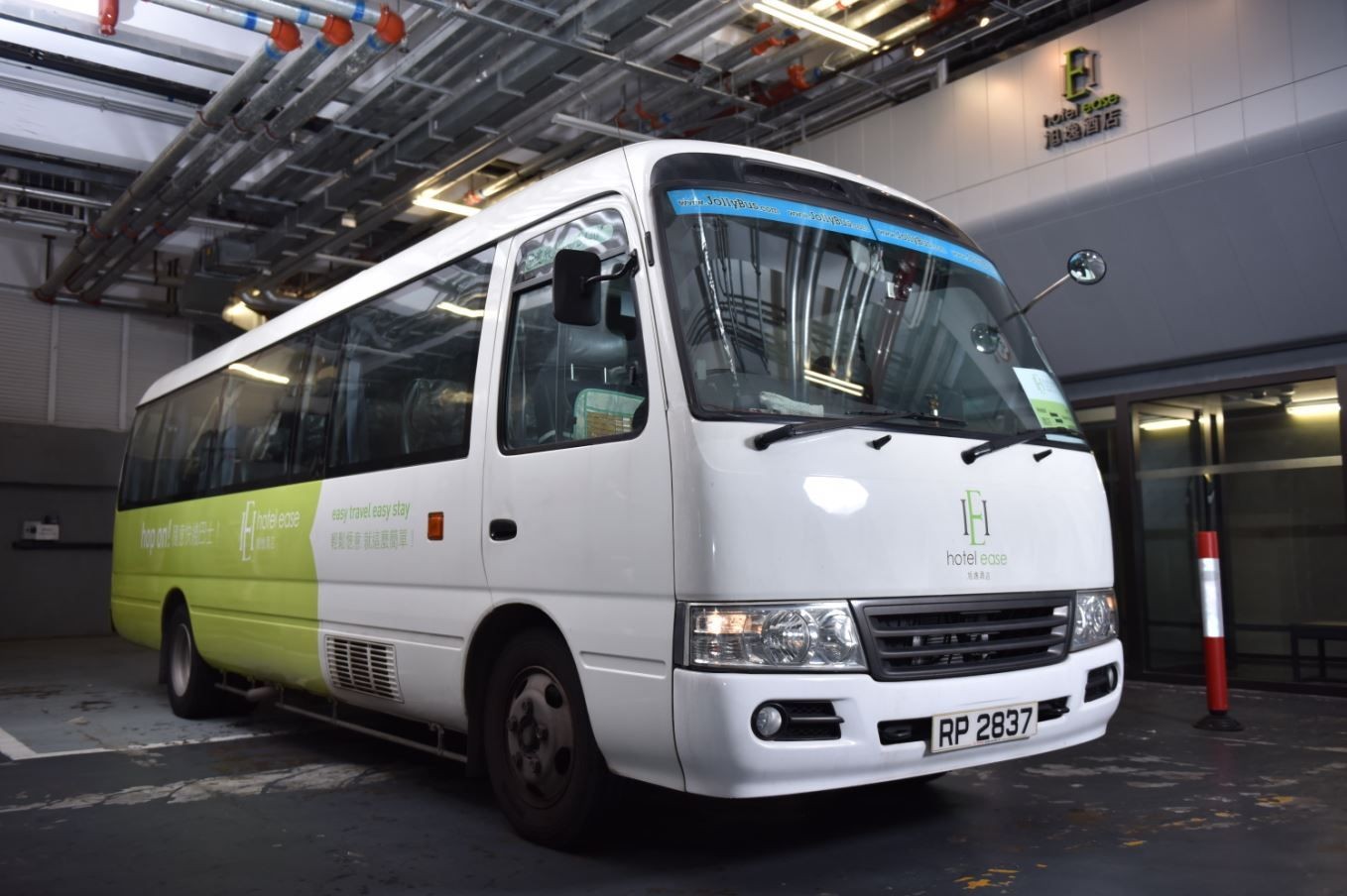 White and green shuttle bus parked in a garage with hotel branding on the side.