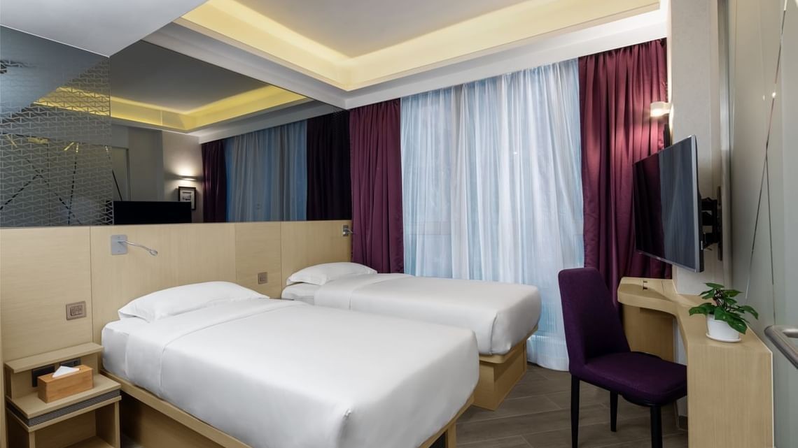 Modern hotel room with two single beds, a wall-mounted TV, and deep purple curtains.