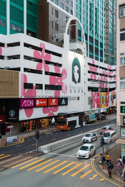 City street view with Panda Hotel, pink floral designs, shops, and passing vehicles.