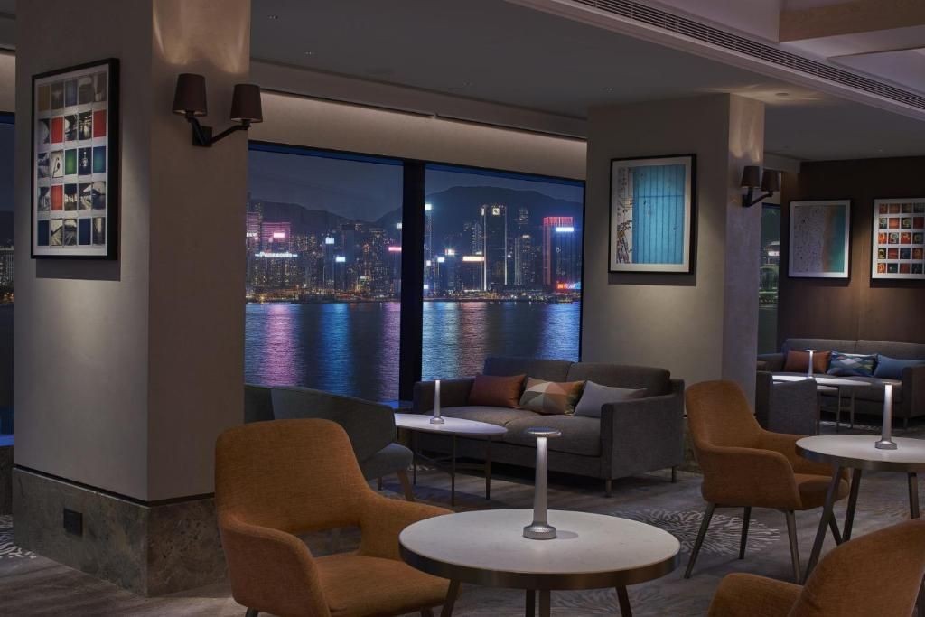Modern lounge with seating and artwork, overlooking city skyline at night through large windows.