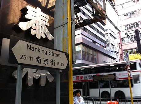 Street sign for Nanking Street in an urban area with a bus and buildings in the background.