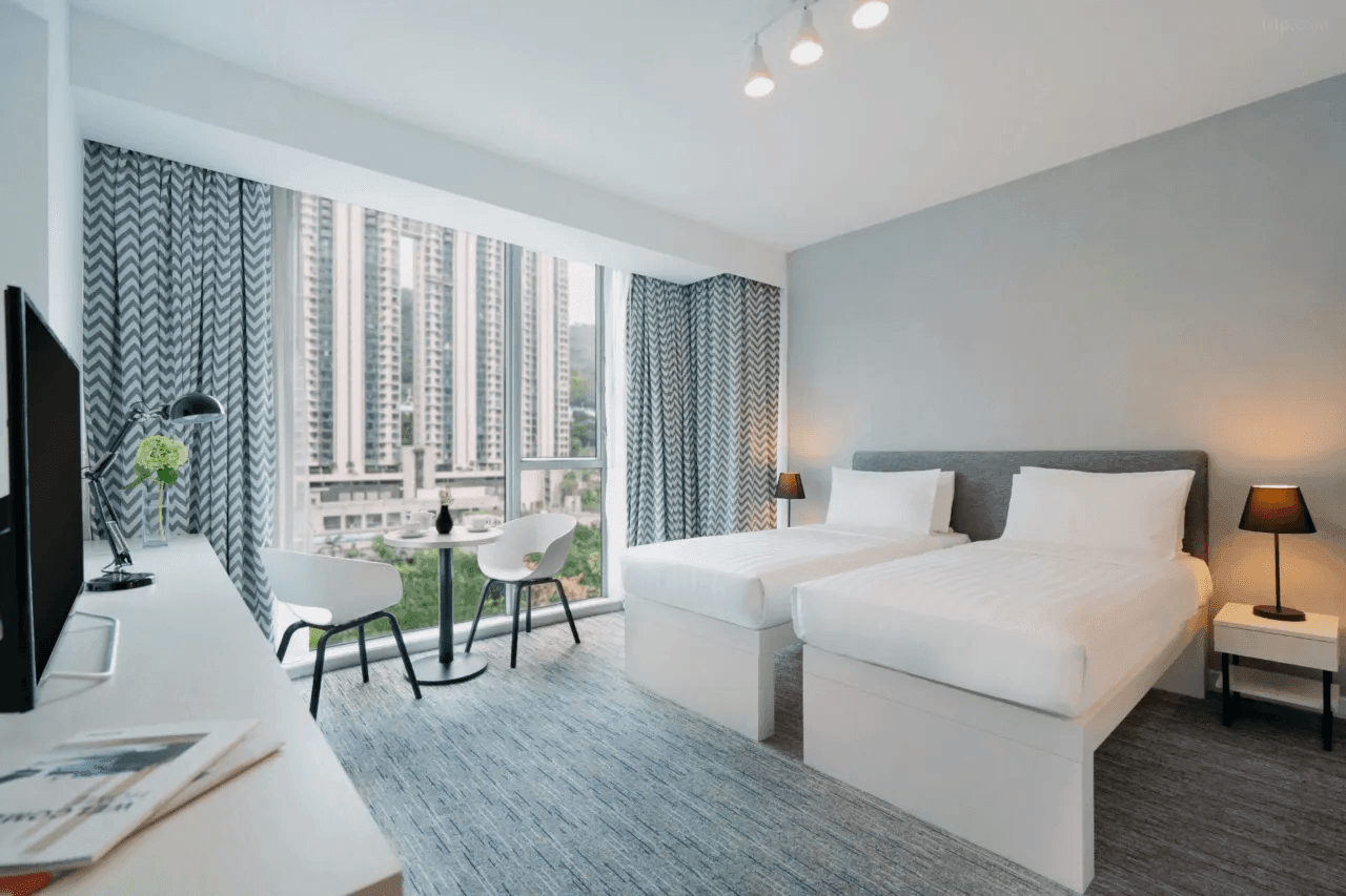 Modern hotel room with two beds, city view window, and minimalist decor.