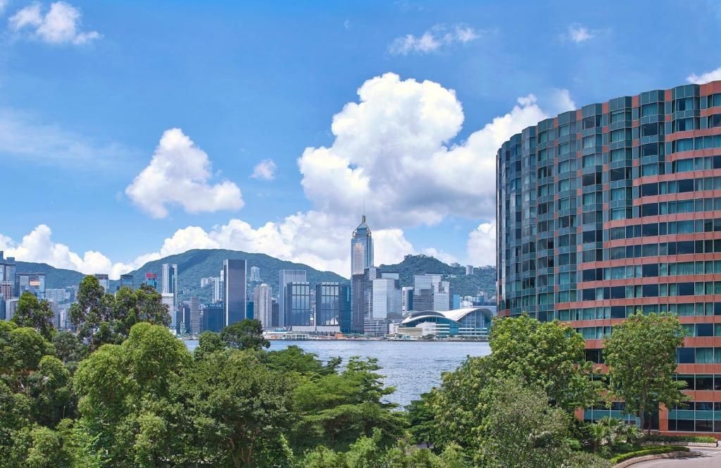 City skyline with modern buildings and a waterfront surrounded by greenery and a blue sky with clouds.