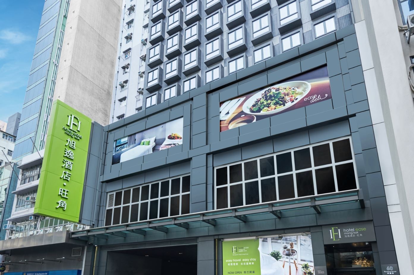 Exterior view of a modern hotel building with a green signboard and large advertisement banners.